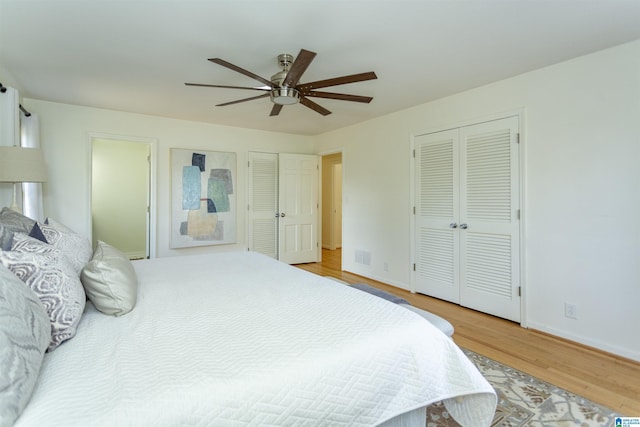 bedroom featuring wood finished floors, visible vents, baseboards, ceiling fan, and two closets