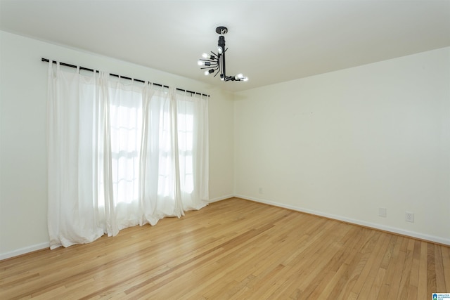 spare room with a chandelier, baseboards, and hardwood / wood-style floors