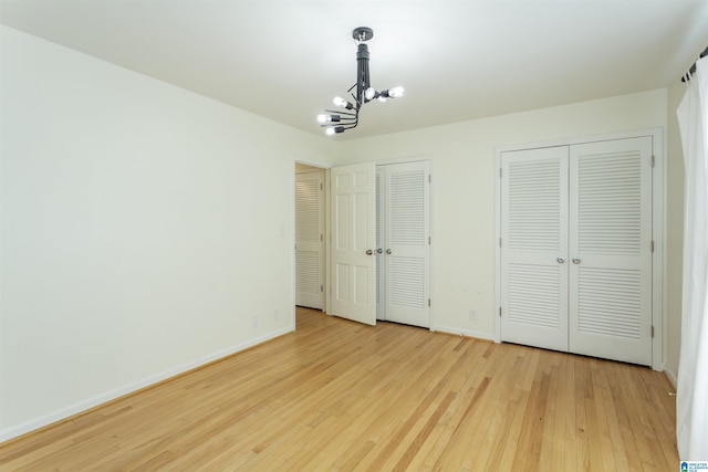 unfurnished bedroom featuring baseboards, light wood-style flooring, two closets, and an inviting chandelier