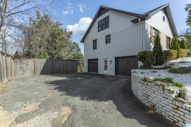 view of property exterior featuring aphalt driveway, brick siding, an attached garage, and fence