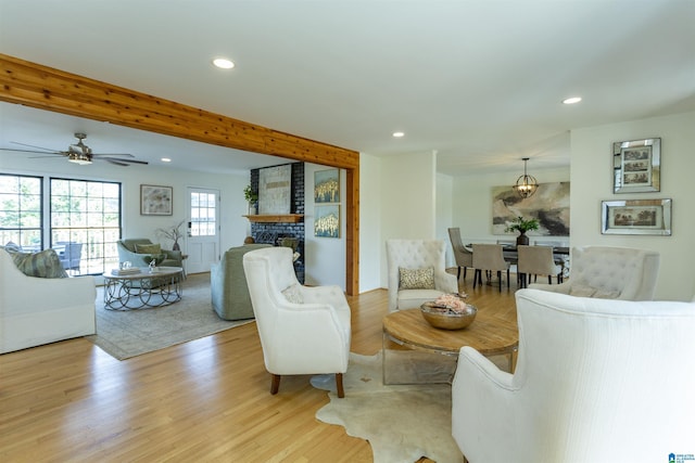 living room featuring beam ceiling, light wood-style flooring, a ceiling fan, recessed lighting, and a stone fireplace