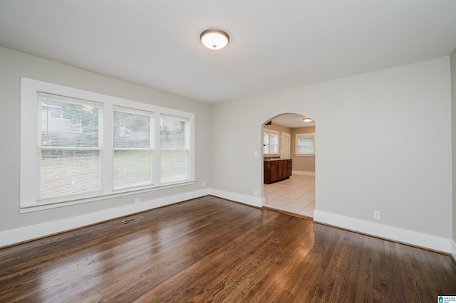 empty room featuring arched walkways, visible vents, baseboards, and wood finished floors