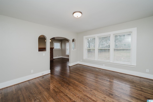 empty room featuring baseboards, visible vents, arched walkways, and wood finished floors