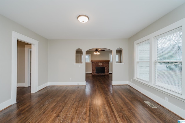 unfurnished living room featuring arched walkways, a brick fireplace, dark wood finished floors, and visible vents