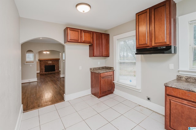 kitchen with arched walkways, baseboards, brown cabinets, and under cabinet range hood