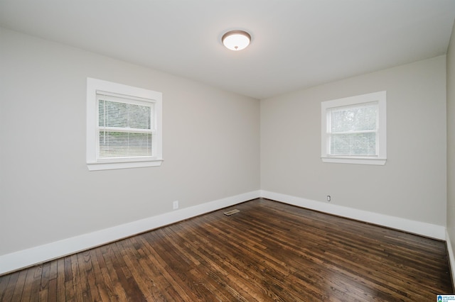 spare room with dark wood-style flooring, visible vents, plenty of natural light, and baseboards