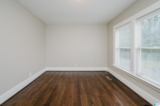 unfurnished room with visible vents, dark wood finished floors, and baseboards