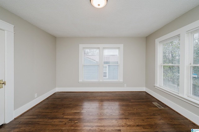 unfurnished room with a wealth of natural light, visible vents, baseboards, and wood finished floors