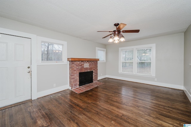 unfurnished living room featuring a brick fireplace, a textured ceiling, visible vents, and wood finished floors