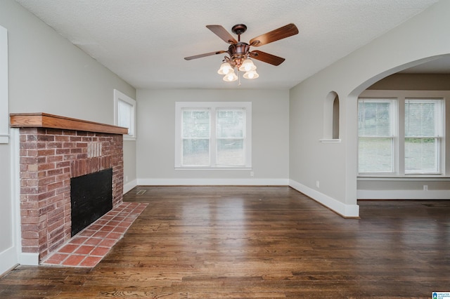 unfurnished living room with a textured ceiling, a brick fireplace, wood finished floors, and baseboards