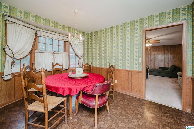 dining area featuring tile patterned floors, wallpapered walls, wainscoting, wooden walls, and ceiling fan with notable chandelier