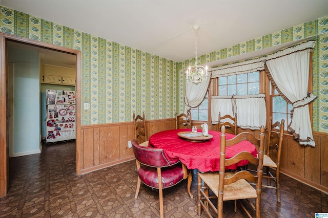 dining room with wooden walls, a wainscoted wall, a notable chandelier, tile patterned floors, and wallpapered walls