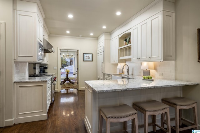 kitchen with light stone countertops, built in appliances, decorative backsplash, a peninsula, and a sink