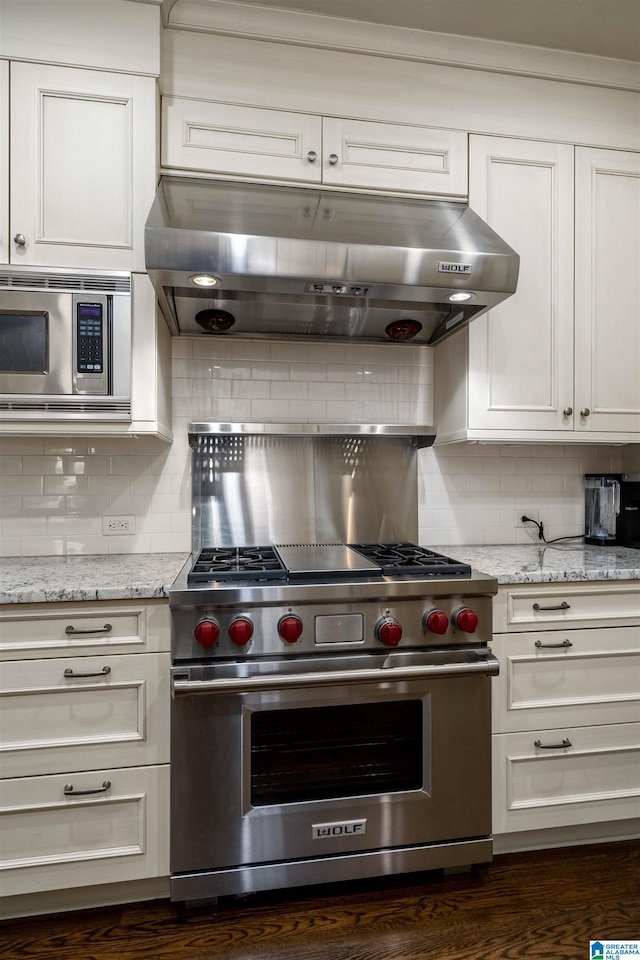 kitchen featuring under cabinet range hood, light stone countertops, tasteful backsplash, and appliances with stainless steel finishes