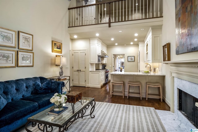 living area with dark wood-style floors, baseboards, recessed lighting, a high end fireplace, and a towering ceiling