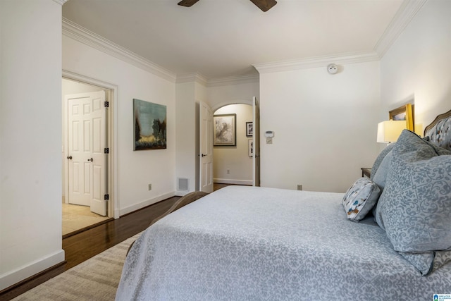 bedroom with visible vents, wood finished floors, arched walkways, crown molding, and baseboards