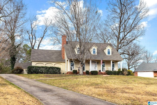 new england style home featuring a front yard, covered porch, a chimney, and stucco siding