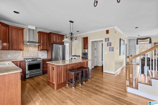 kitchen with a center island, appliances with stainless steel finishes, light wood-style floors, ornamental molding, and wall chimney exhaust hood