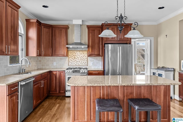 kitchen featuring a sink, light wood-style floors, appliances with stainless steel finishes, wall chimney range hood, and crown molding