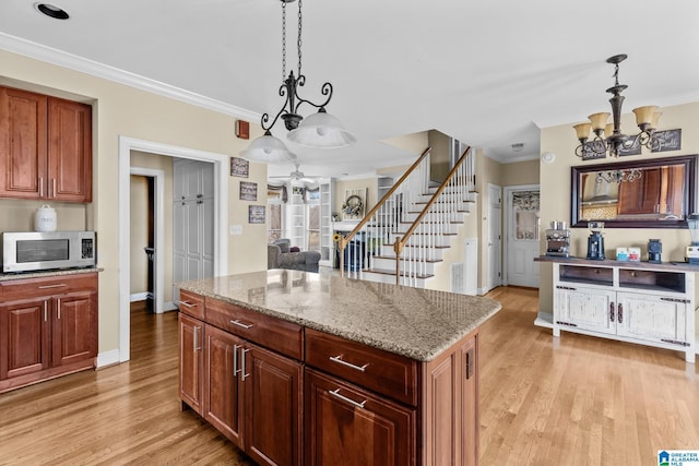 kitchen featuring ornamental molding, pendant lighting, stainless steel microwave, and light wood-style floors