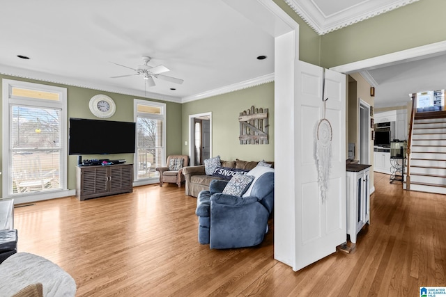 living area with ornamental molding, wood finished floors, ceiling fan, and stairs