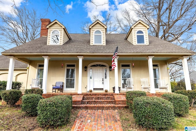 cape cod home featuring covered porch, roof with shingles, and a chimney