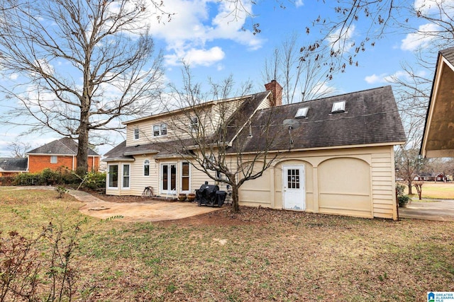 back of property with a shingled roof, a chimney, a patio area, and a lawn