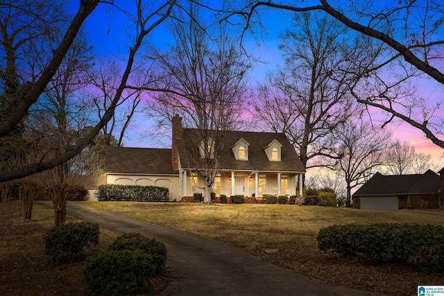 cape cod home with a chimney, a porch, an attached garage, a front yard, and driveway