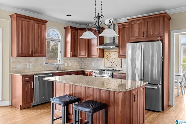 kitchen featuring a sink, ornamental molding, wall chimney range hood, appliances with stainless steel finishes, and light wood finished floors