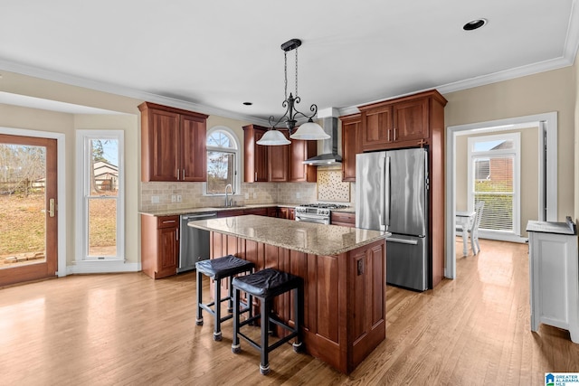 kitchen with wall chimney exhaust hood, appliances with stainless steel finishes, a kitchen island, and light wood-style flooring