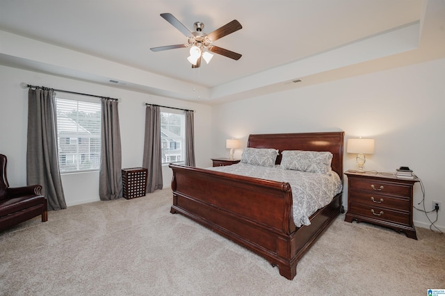 bedroom with a tray ceiling, light colored carpet, ceiling fan, and visible vents