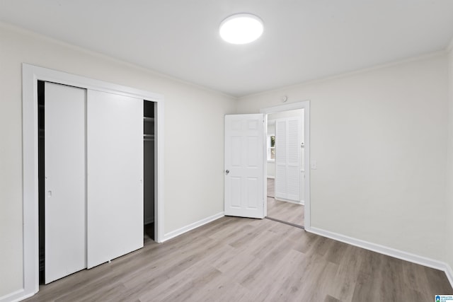 unfurnished bedroom with ornamental molding, a closet, light wood-type flooring, and baseboards