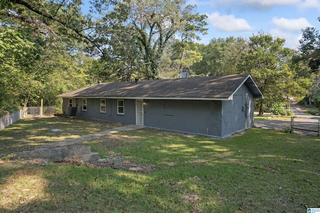 rear view of property featuring stucco siding, central AC, a lawn, and fence