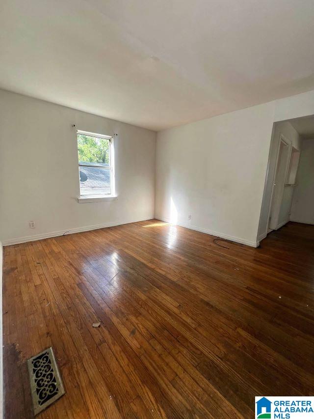 spare room featuring wood-type flooring, visible vents, and baseboards