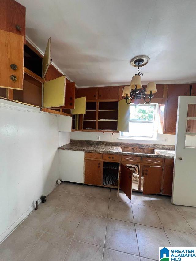 kitchen with light tile patterned floors, dark countertops, brown cabinets, an inviting chandelier, and open shelves