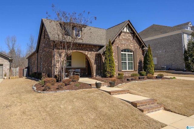 view of front of property featuring a shingled roof, a front yard, and brick siding