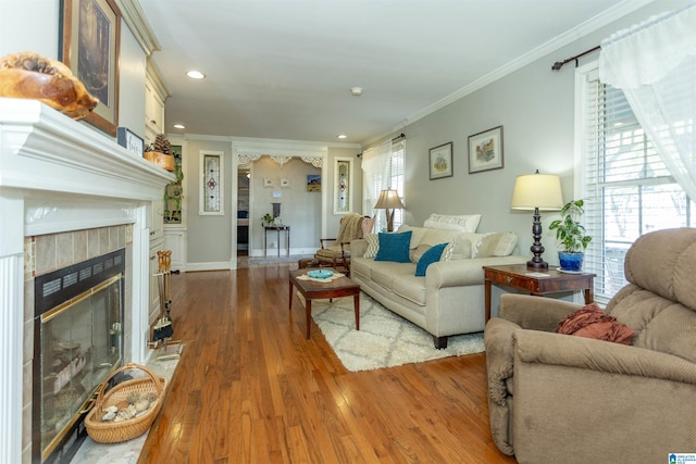 living room with a tile fireplace, recessed lighting, wood finished floors, baseboards, and crown molding