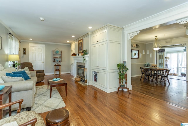 living room featuring baseboards, ornamental molding, wood finished floors, a fireplace, and recessed lighting