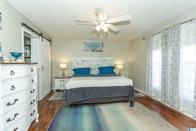 bedroom with dark wood-type flooring, multiple windows, a textured ceiling, and a barn door