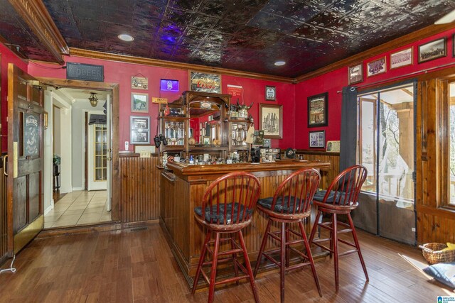 bar with an ornate ceiling, crown molding, a bar, and wood finished floors