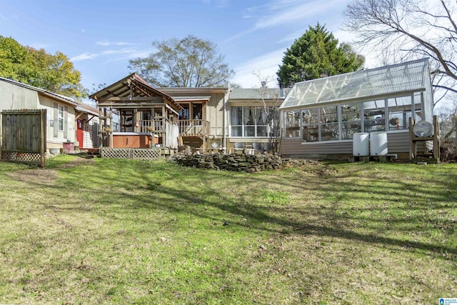 rear view of property with a sunroom, a hot tub, a lawn, and a deck