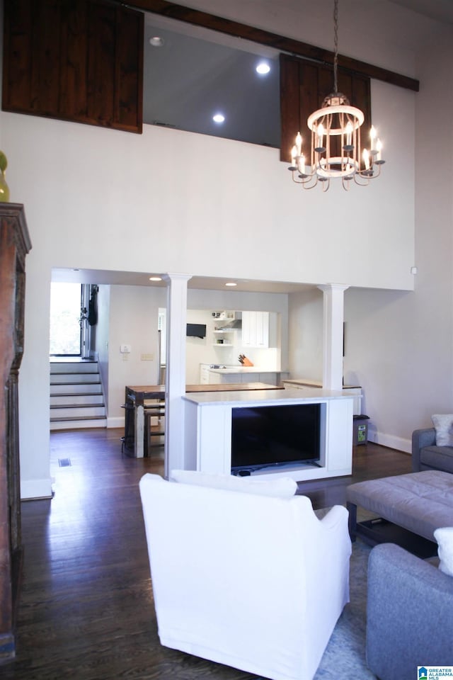 living room with dark wood-style flooring, stairway, a towering ceiling, an inviting chandelier, and baseboards