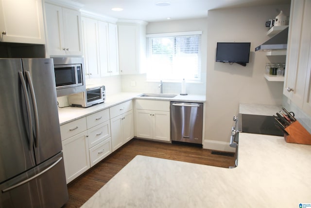 kitchen with stainless steel appliances, a sink, light countertops, wall chimney exhaust hood, and dark wood finished floors