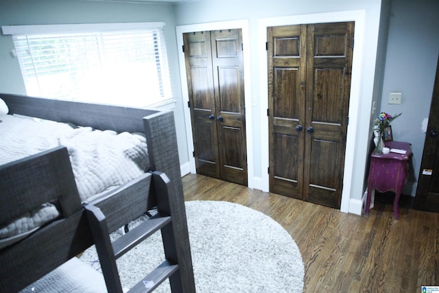 bedroom with two closets, baseboards, and wood finished floors