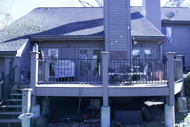 rear view of property with a deck, roof with shingles, a chimney, and stairs