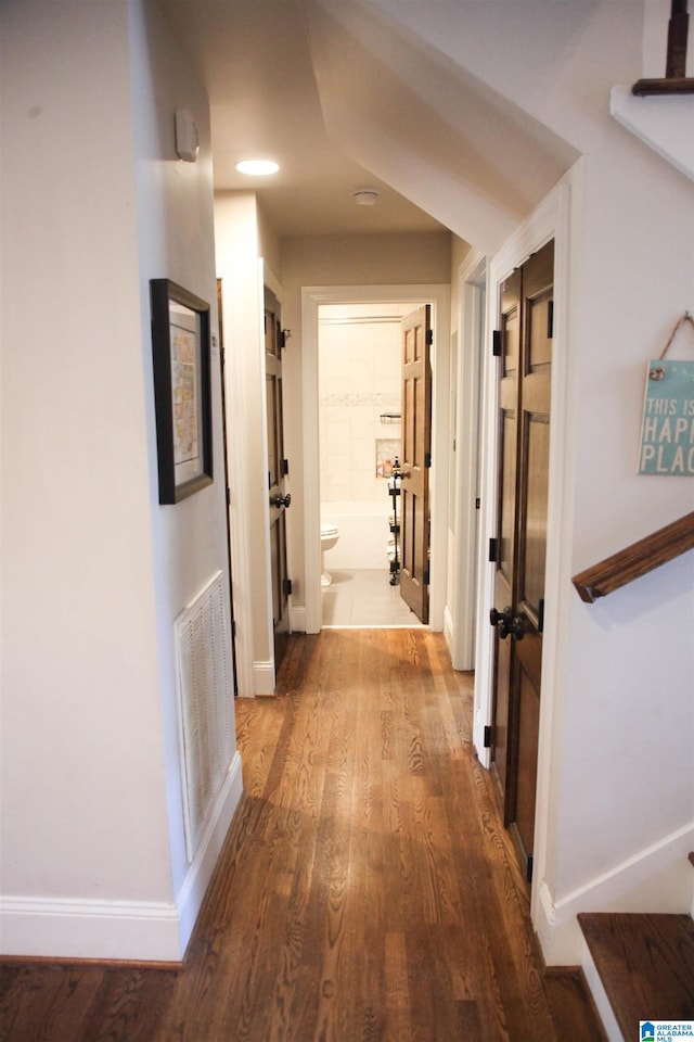 hallway featuring baseboards, visible vents, and wood finished floors