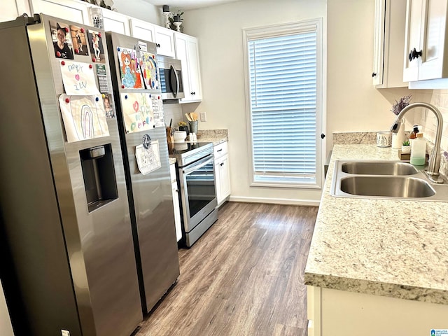 kitchen with light countertops, stainless steel appliances, wood finished floors, white cabinetry, and a sink