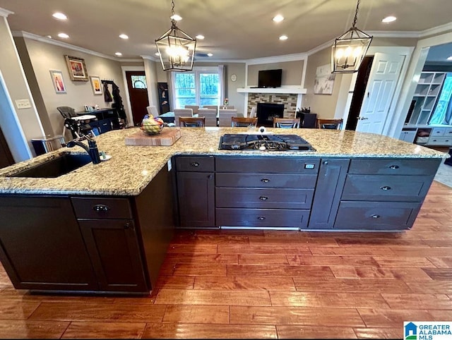 kitchen with wood finished floors, gas stovetop, a fireplace, a sink, and recessed lighting