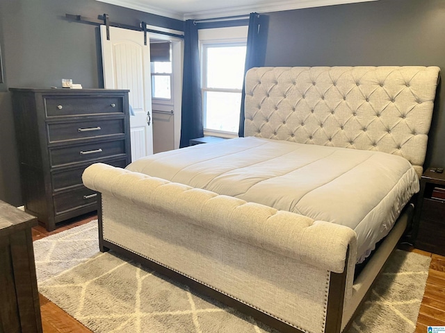 bedroom with ornamental molding, wood finished floors, and a barn door