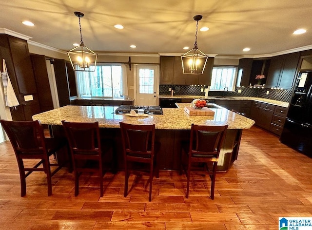 kitchen with a large island, ornamental molding, wood finished floors, stainless steel gas cooktop, and a sink